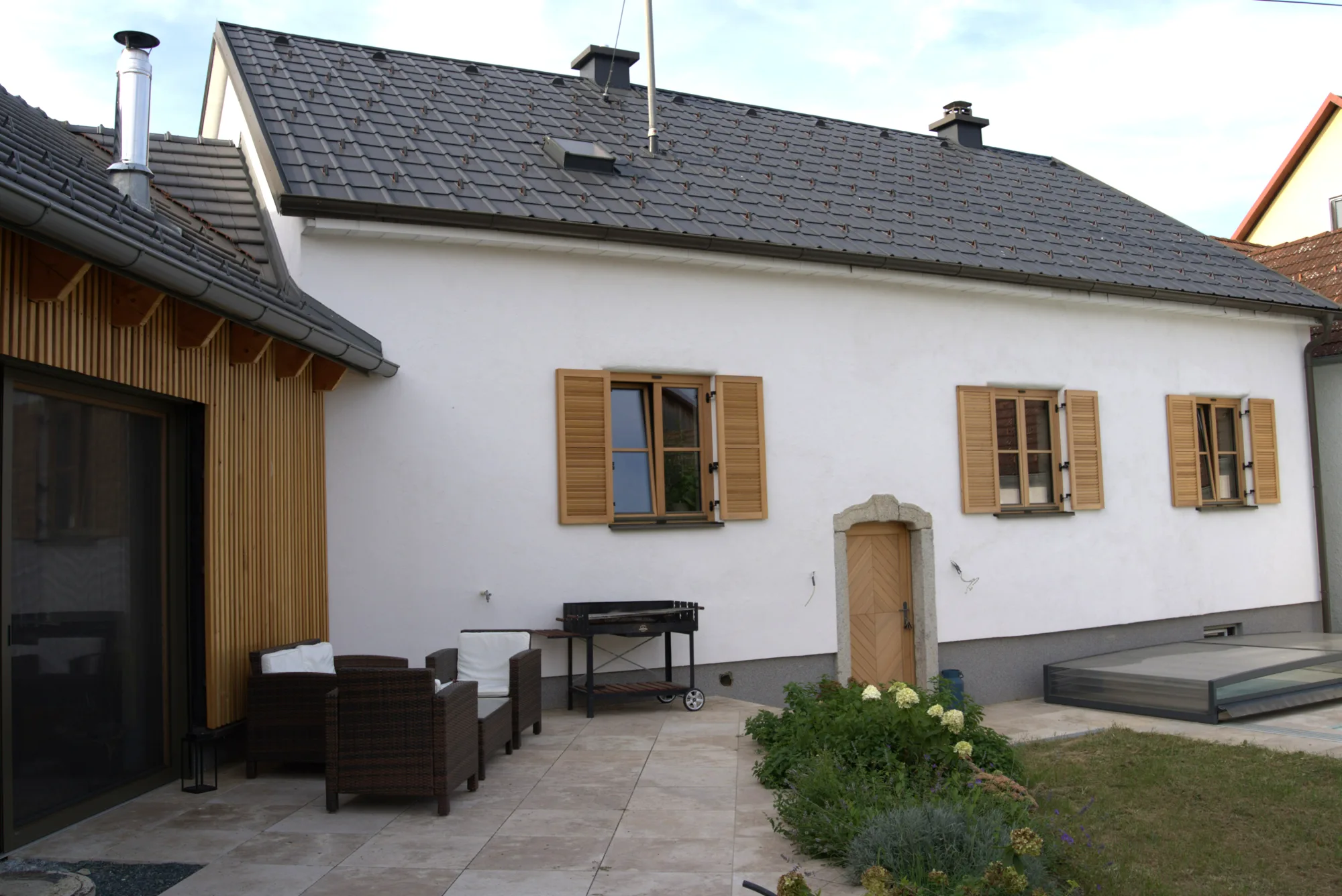 Straßenansicht: weißer Putz, Holzfensterläden, Ziegeldach, rechts der Holzzubau.