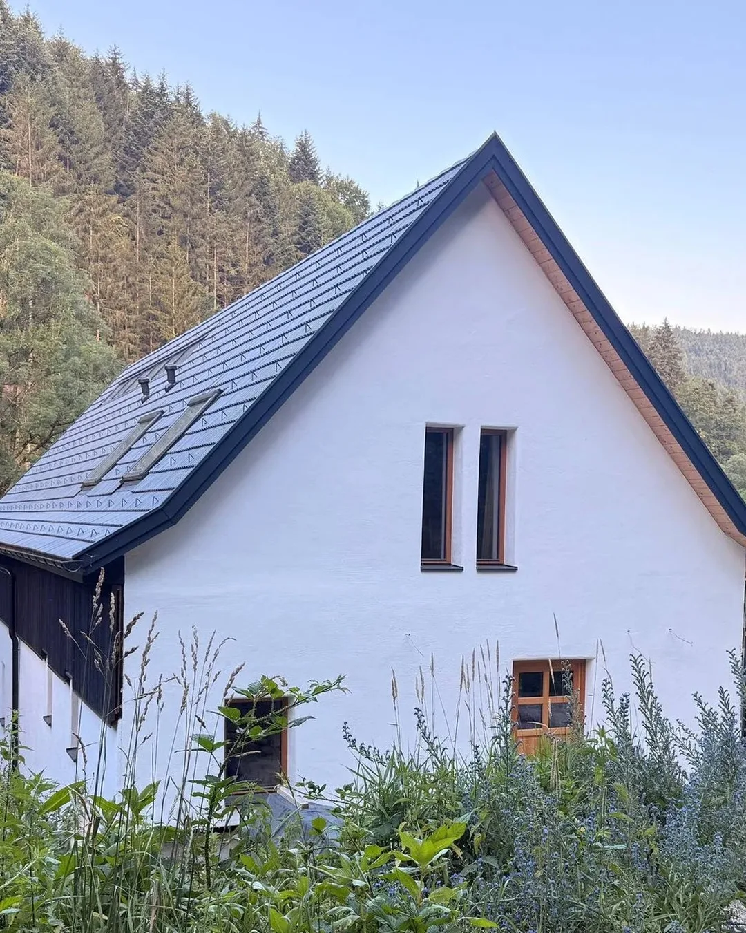 Dieselbe Ansicht nach der Sanierung: weißer Putz, neues Dach mit Photovoltaik, zwei schmale Giebelfenster.