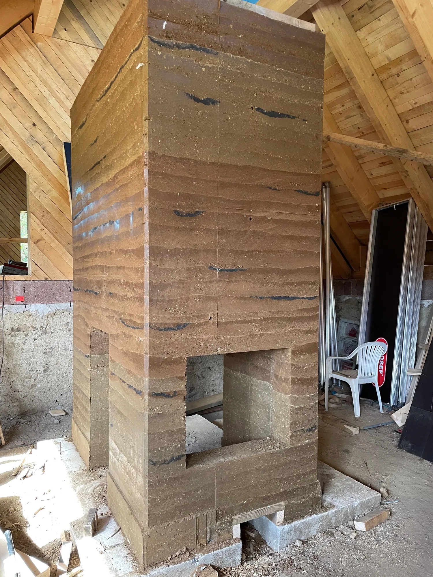 Fertig gestampfter Ofen aus Lehm mit sichtbaren Schichten, unter dem neuen Holzdachstuhl.