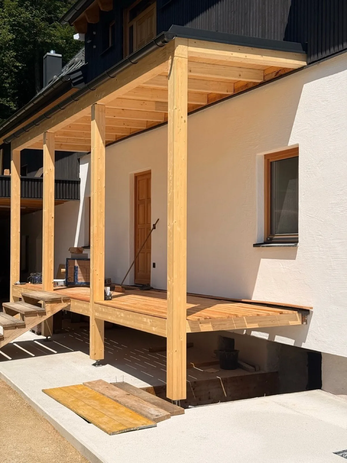 Neue Veranda aus Holz vor dem weiß verputzten Bestand.